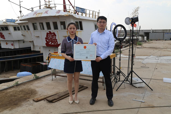 海鮮電商張夢琴與幫辦員手持食品經(jīng)營許可證合影。贛榆區(qū)委宣傳部供圖