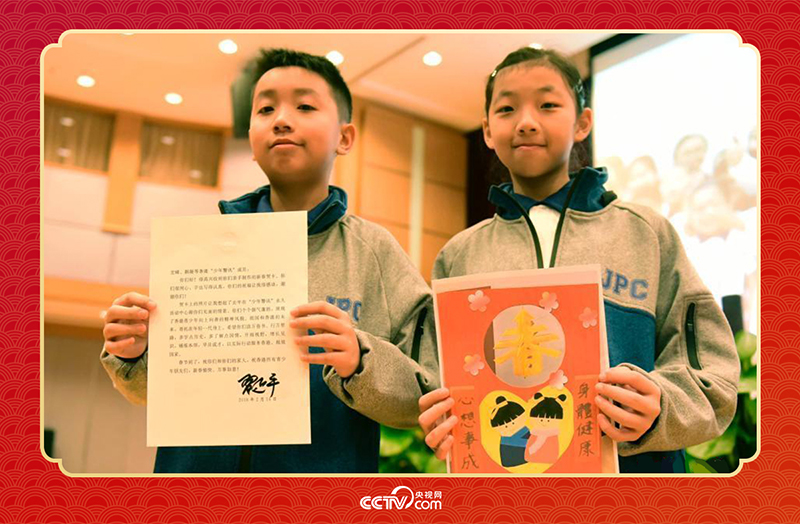 圖為香港“少年警訊”成員郭宏晞（左）展示習(xí)主席回信、羅顥凝（右）展示送給習(xí)主席的賀卡并合影。