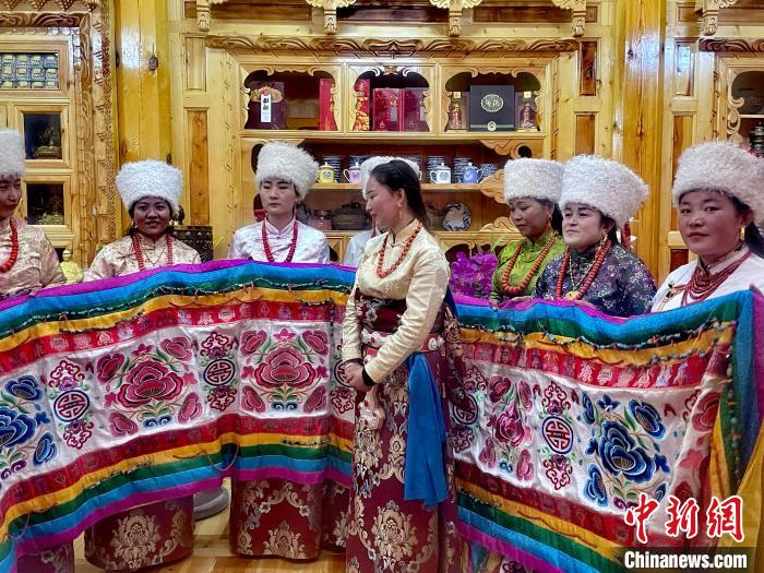 圖為女性展示村民自發(fā)繡制的“百米五彩哈達(dá)”。　李玉峰 攝